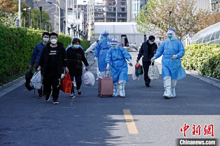 康复者带着自己的行李，在医护人员的陪伴下走出方舱医院。　殷立勤 摄