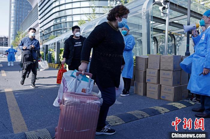 康复者带着自己的行李，在医护人员的陪伴下走出方舱医院。　殷立勤 摄