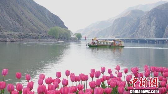 图为河中的游船和岸边的红花。　侯奇志 摄