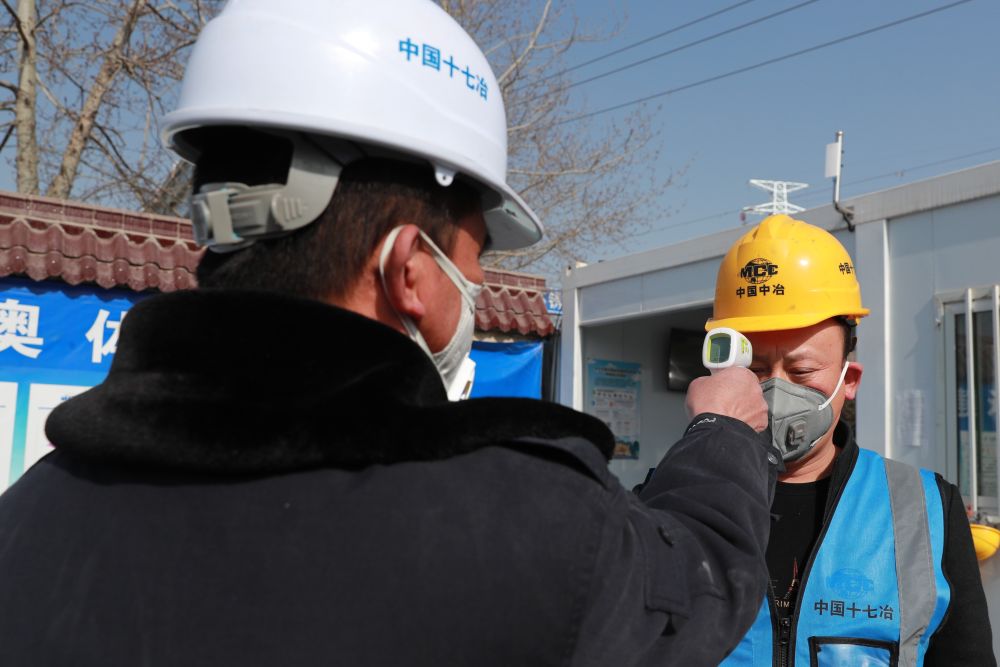 工作人员对进入兰州市奥体中心项目建设工地的建筑工人测量体温